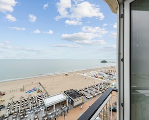 A beachside view from a balcony overlooking a beach with a pier in the distance, a lifeguard tower, and a row of beachside restaurants.