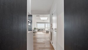 A modern hallway with a wooden floor, leading to a kitchen and a living area with a large window. - Attractive Studio With a Sea-view (Blankenberge)