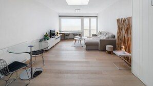 A modern living room with a glass dining table, a sofa, and a TV. - Attractive Studio With a Sea-view (Blankenberge)