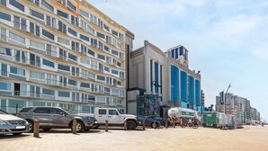 A multi-story building with balconies, parked cars, and a construction site with a green container. - Attractive Studio With a Sea-view (Blankenberge)