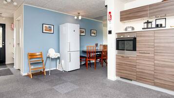 Een kleine keuken met een koelkast, oven en magnetron. Er is een eethoek met een tafel en stoelen.