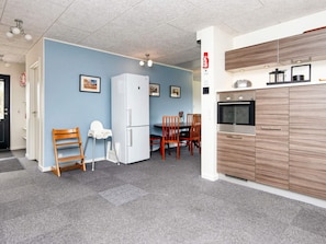 A compact kitchen with a refrigerator, oven, and microwave. There is a dining area with a table and chairs. - 5 Star Holiday Home in Glesborg (Glesborg)