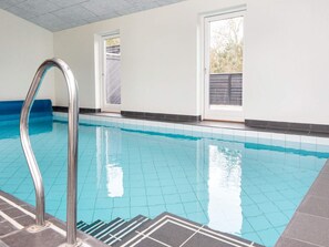 An indoor swimming pool with clear blue water, a metal ladder, and a view of the outside through a window. - 5 Star Holiday Home in Glesborg (Glesborg)