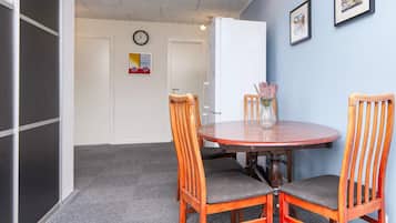 Ein Zimmer mit einem runden Holztisch, zwei Holzstühlen, einer Blumenvase, einer Wanduhr und gerahmten Bildern.
