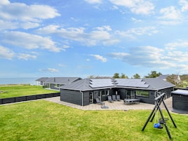 A modern building with a flat roof, outdoor seating area, and a swing set.