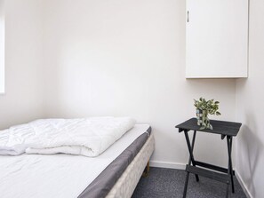 Un lit simple avec une couette blanche et une tête de lit grise, dans une pièce aux murs blancs.
