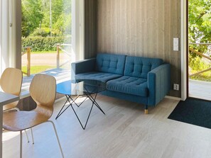 A modern living room with a blue sofa, a glass coffee table, and a wooden chair. - 4 Star Holiday Home in Henan (Henån)