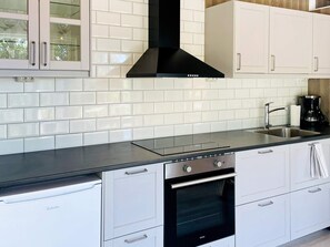 Una cocina moderna con armarios blancos, una campana extractora negra, un lavamanos de acero inoxidable y una cafetera.