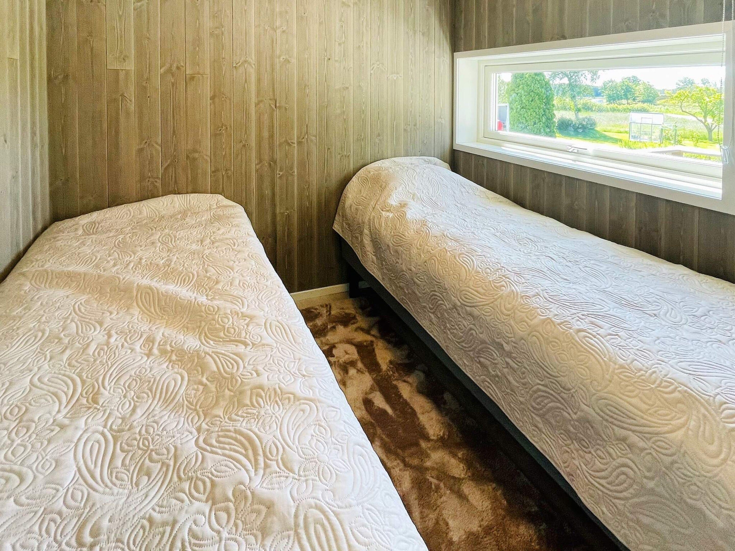 Un dormitorio con dos camas individuales, una ventana con vistas a la vegetación y paneles de madera en las paredes.