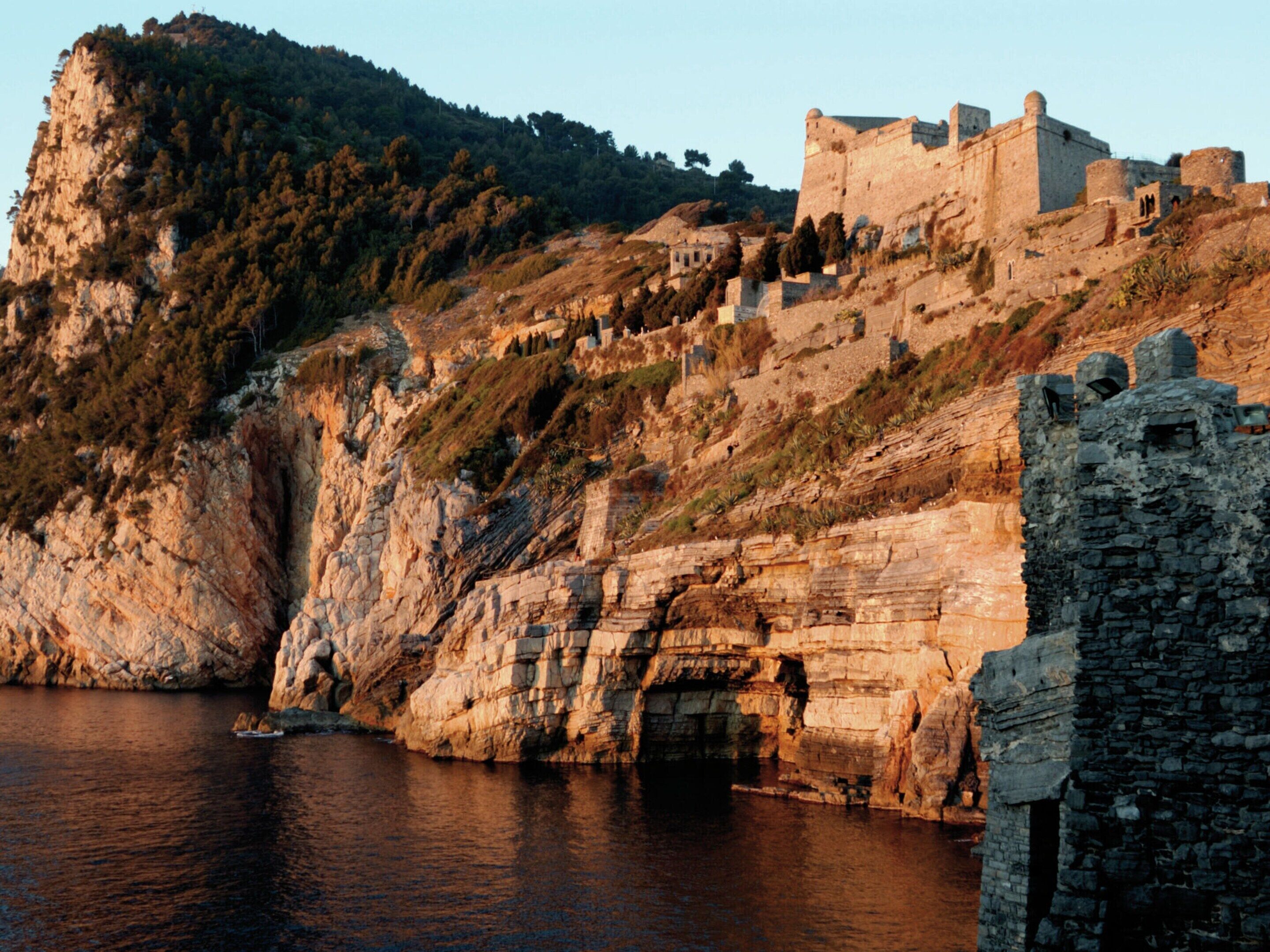 A coastal castle with a fortified structure, a rocky cliff, and a body of water.