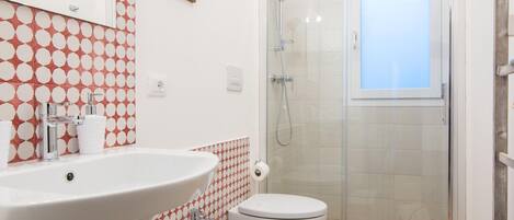 Un baño con lavamanos, dos inodoros, ducha y pared con diseño.