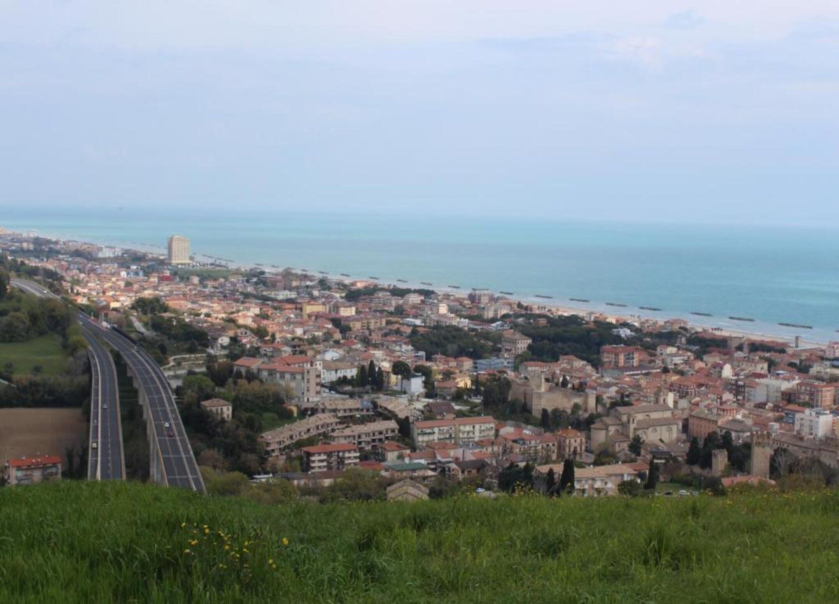 A coastal cityscape with a highway curving through it, buildings, and a beach.