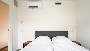Une chambre à coucher comprenant un lit, deux tables de chevet, un appareil de climatisation et une bouche d’aération fixée au mur.