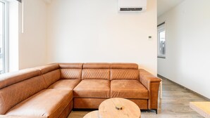 Un salon moderne avec un canapé d’angle, une table basse ronde en bois et un climatiseur fixé au mur.