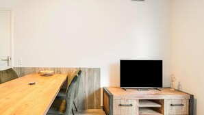 Un salon moderne avec une table à manger en bois, un téléviseur à écran plat posé sur un meuble en bois, et un design minimaliste.