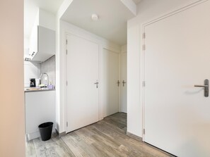 A hallway with white doors, a kitchen area with a sink, and a black trash bin. - Airy Apartment in South Limburg (Landgraaf)