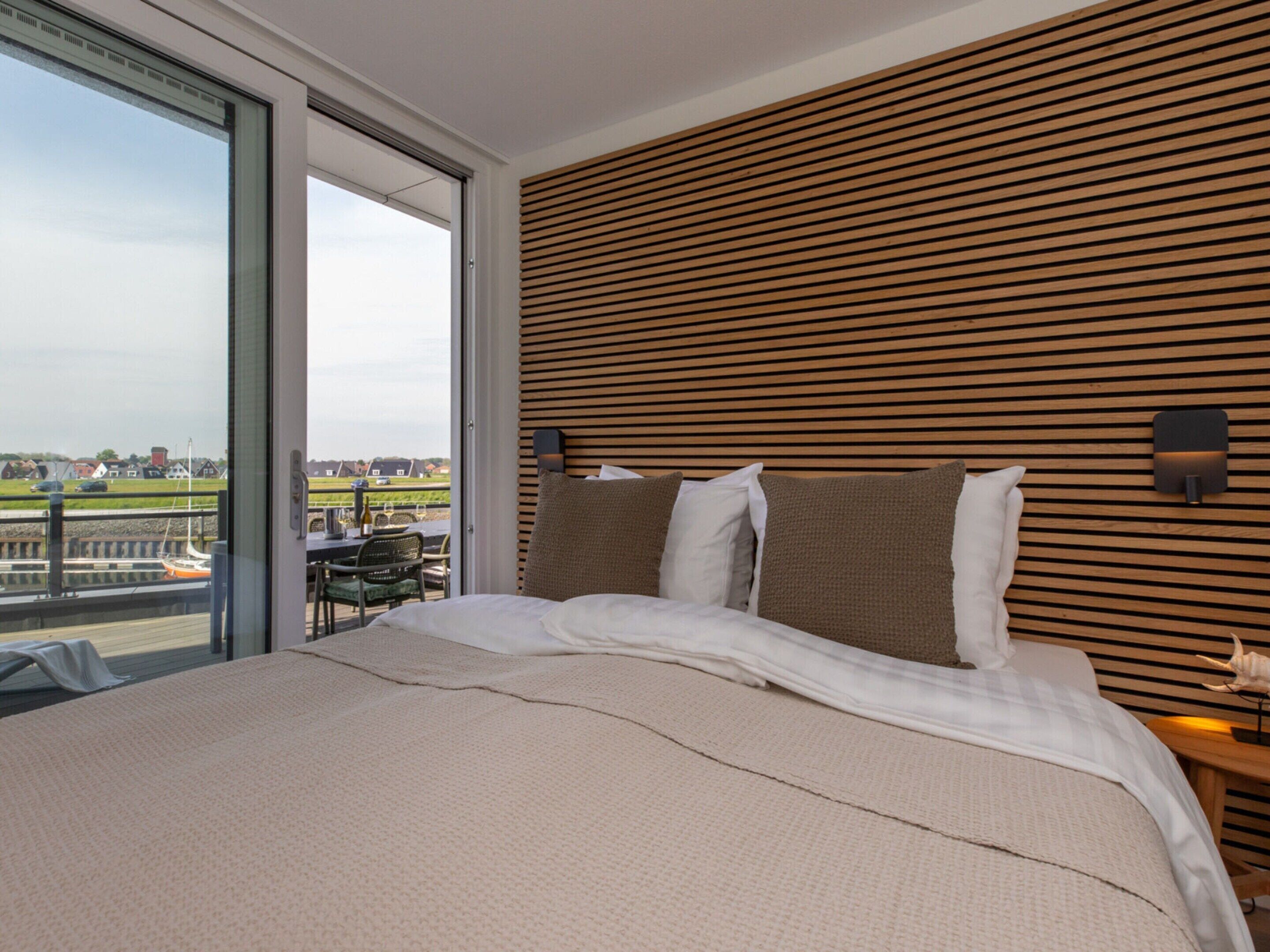 A modern hotel room with a large bed, wooden headboard, and a view of a marina.