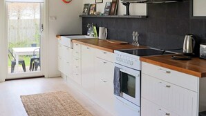 A modern kitchen with white cabinetry, a wooden countertop, a built-in oven, and a black backsplash. - 4 Star Holiday Home in Halmstad (Halmstad)