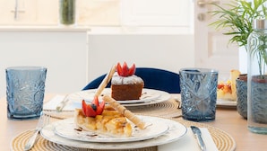 Una mesa de comedor con platos de comida, dos vasos azules con diseño y un florero con una planta.