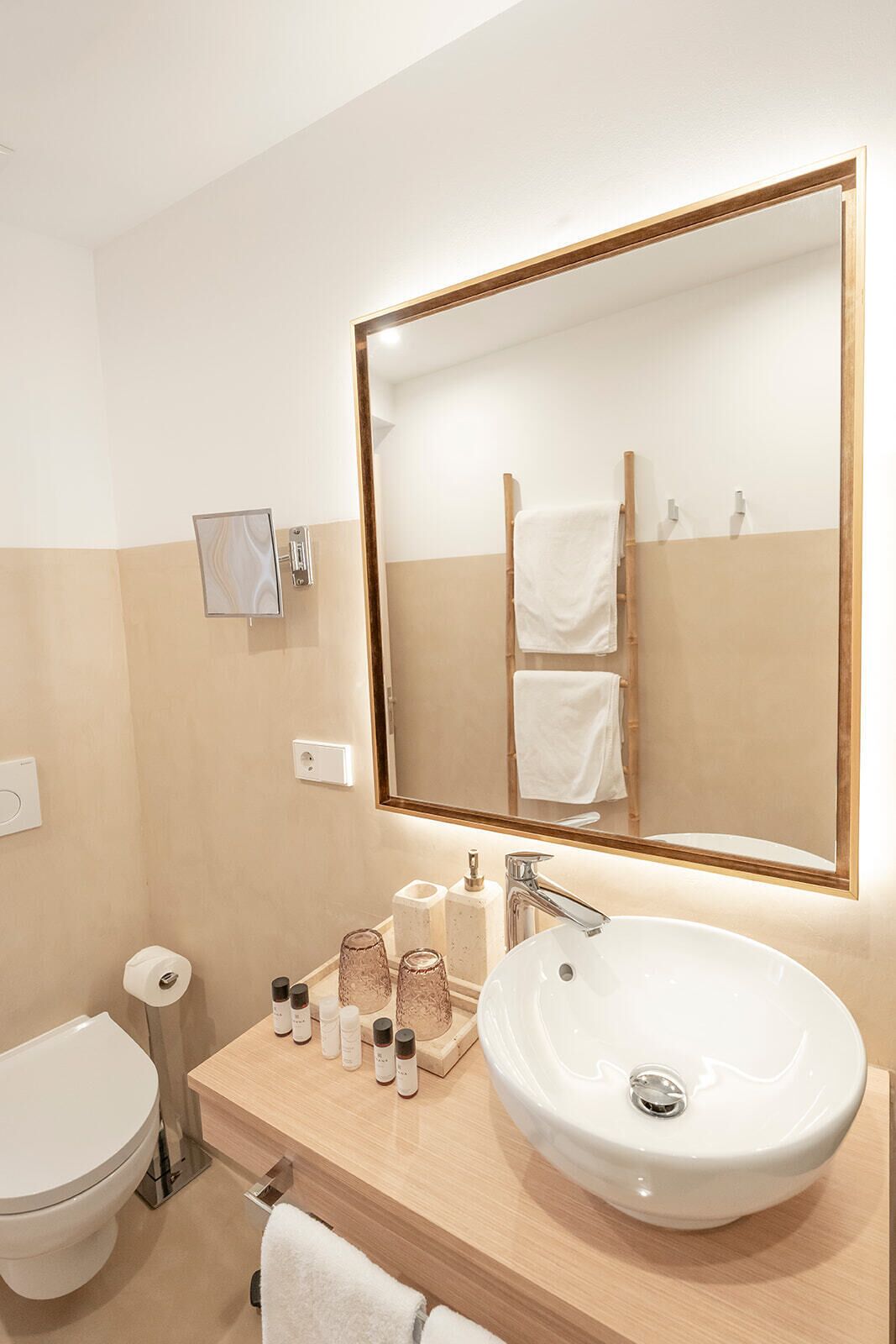 Un baño con un espejo grande, un lavabo con artículos de aseo y un inodoro.