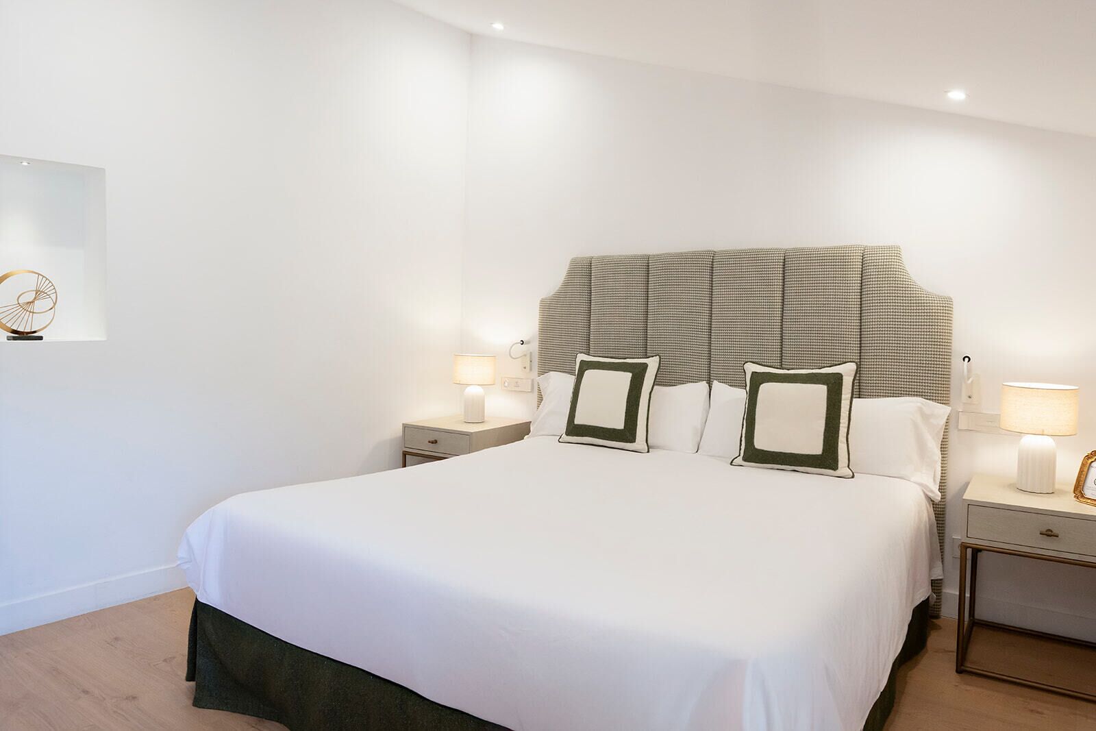 Cama bem arrumada com lençóis brancos, duas mesas de cabeceira com luminárias e cabeceira com padrão xadrez.