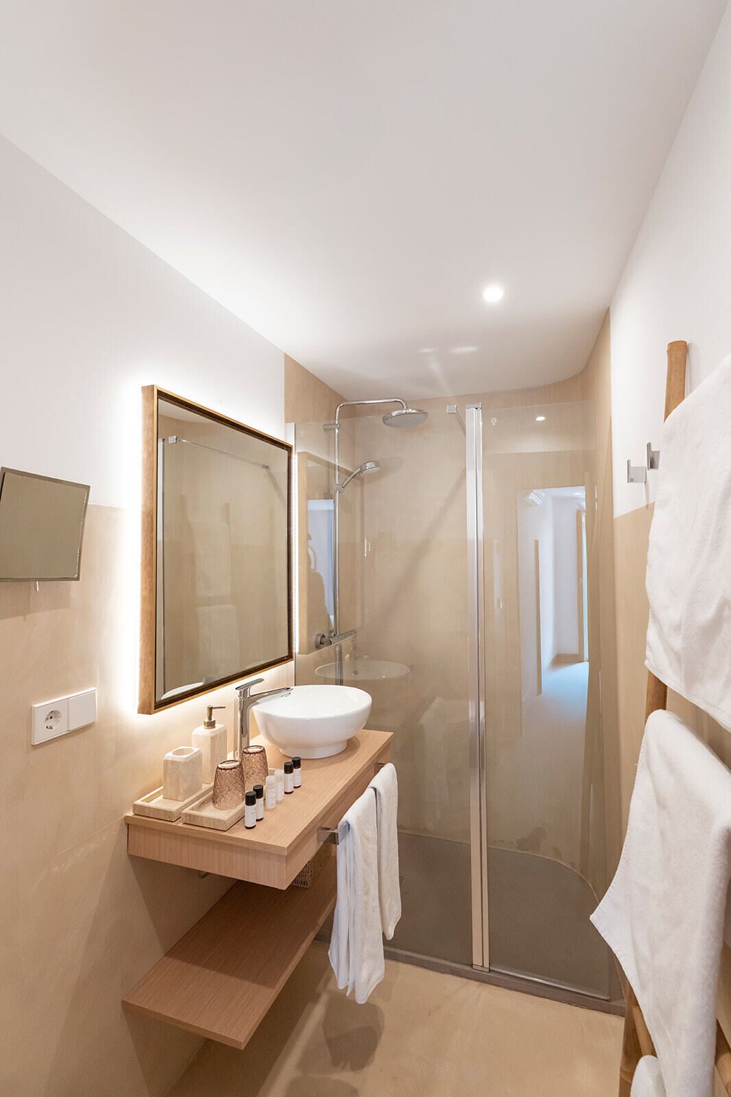A modern bathroom with a glass-enclosed shower, a large mirror, and a wooden vanity with toiletries.
