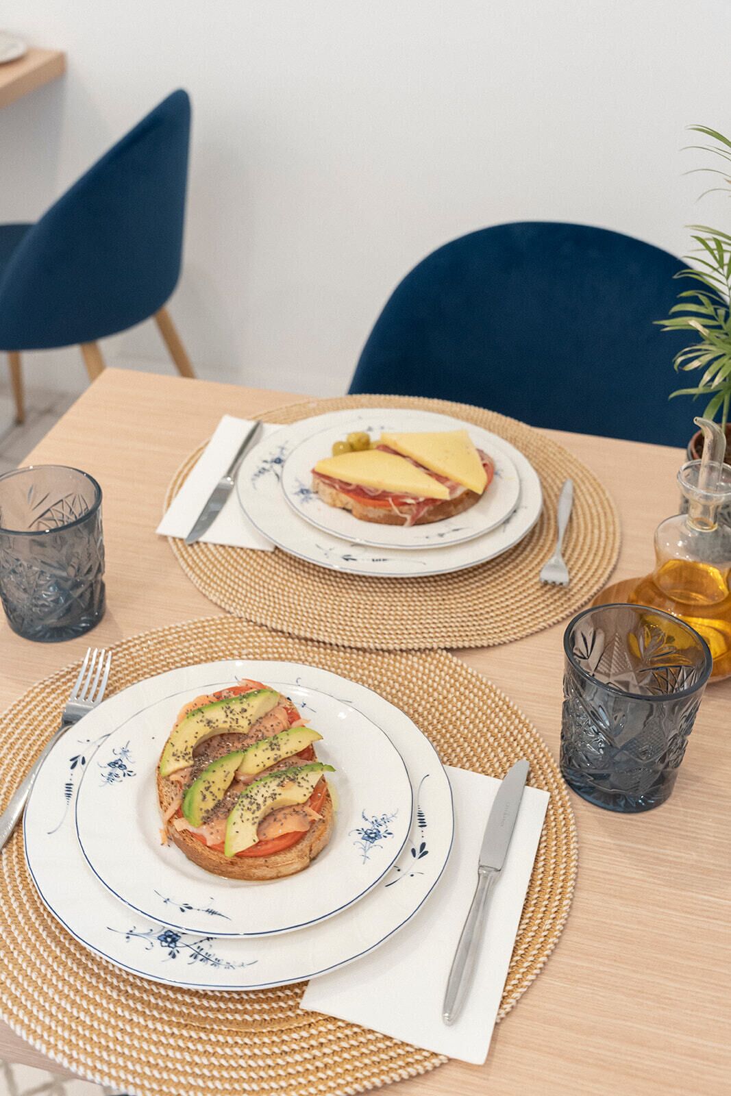 Una mesa de comedor con dos platos de sándwiches, cubiertos y vasos.