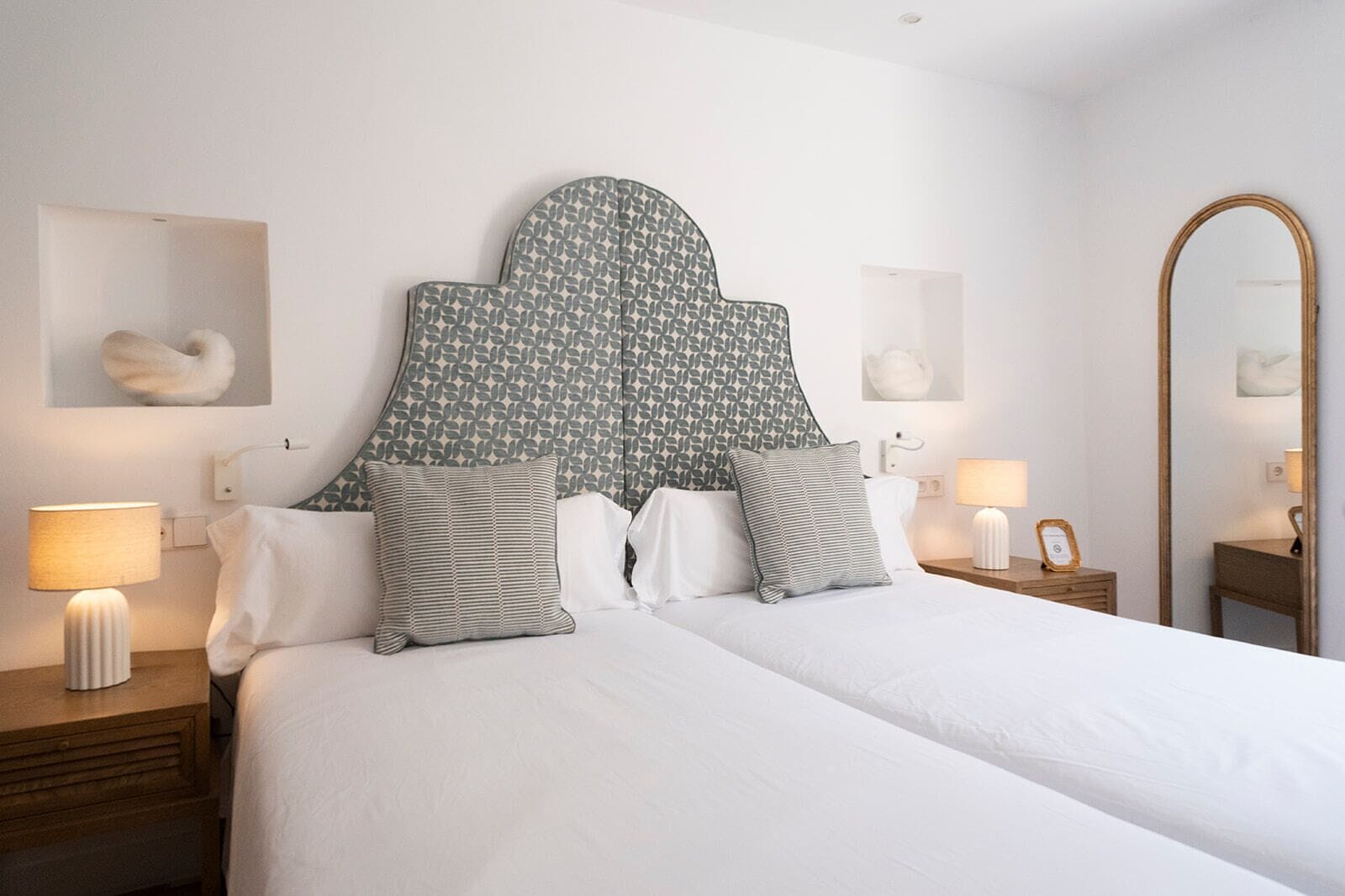Una habitación de hotel con una cama grande, dos mesitas de noche, un espejo y una lámpara fijada a la pared.