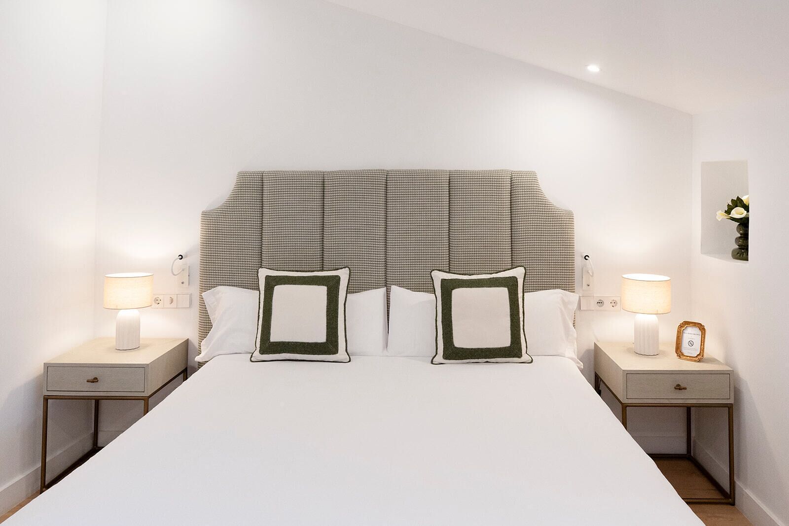 Un dormitorio ordenado con una cama grande, dos mesitas de noche con lámparas y un cabecero.