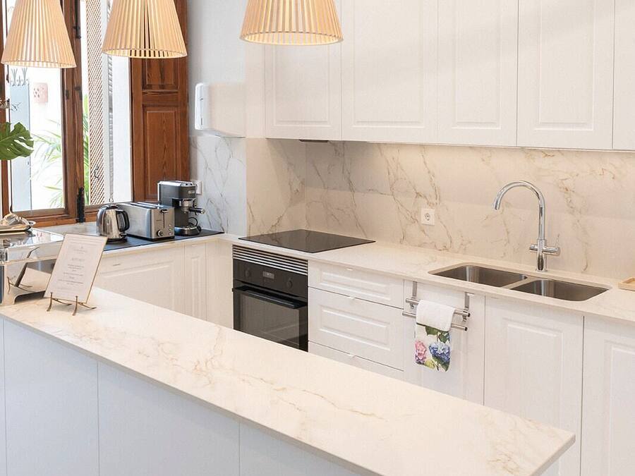 Una cocina moderna con armarios blancos, encimera de mármol, horno empotrado, un lavabo y tres lámparas colgantes.