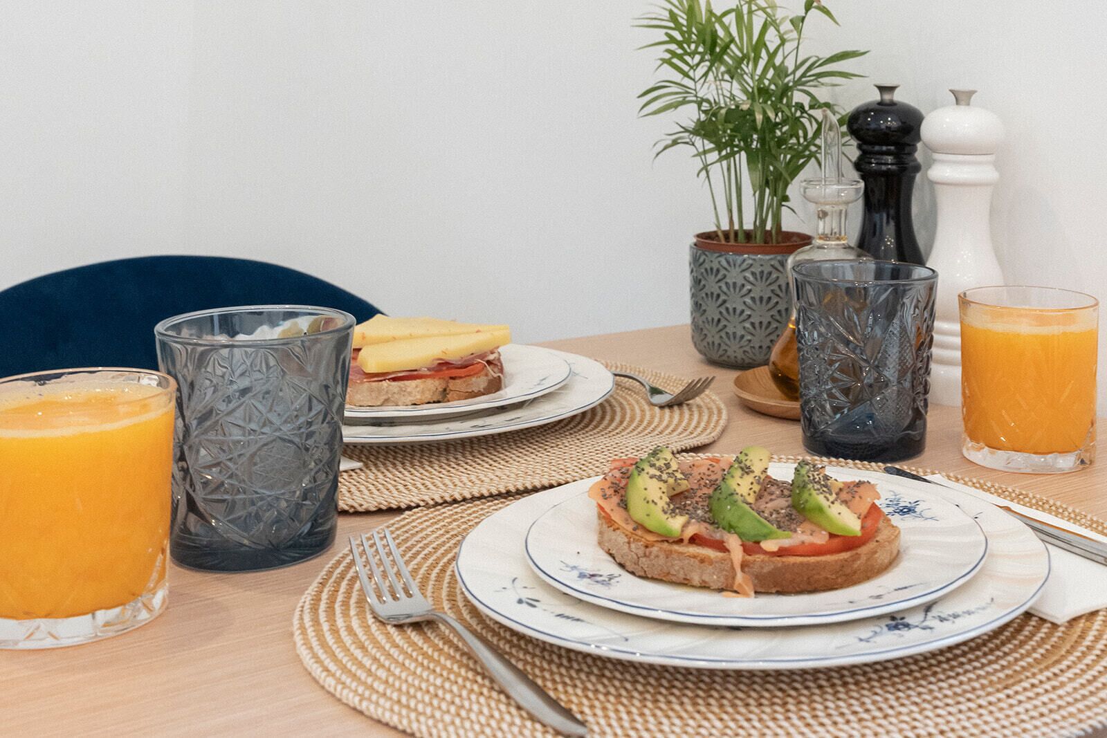 A breakfast setting with two plates of food, two glasses of orange juice, a fork, and a knife on a table with a woven placemat.