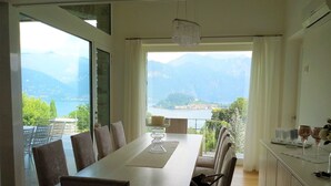 A dining area with a long table, chairs, and a view of mountains and a lake. - The Great Beauty, beautiful property with amazing view on the lake of Como (Lombardia)