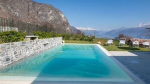 A rectangular pool with clear blue water, surrounded by a stone wall and a metal fence, with a mountainous backdrop. - The Great Beauty, beautiful property with amazing view on the lake of Como (Lombardia)