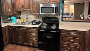 A kitchen with wooden cabinets, a microwave, stove, and a sink. - Large 1 Bedroom Apartment in the Heart of Quidi Vidi (Ground Level) (St. John's)