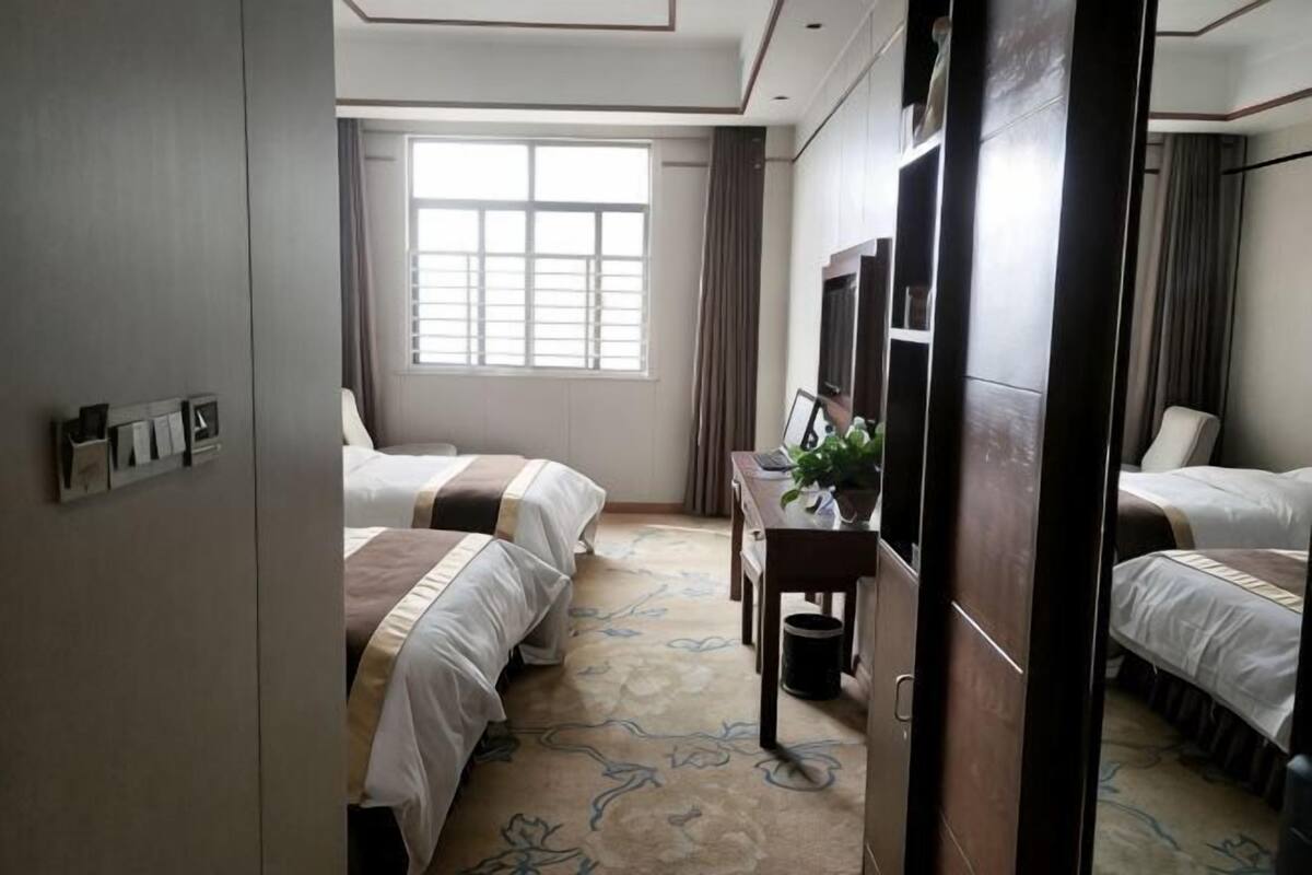 Una habitación de hotel con dos camas, un escritorio con una planta, un televisor y una ventana con cortinas.