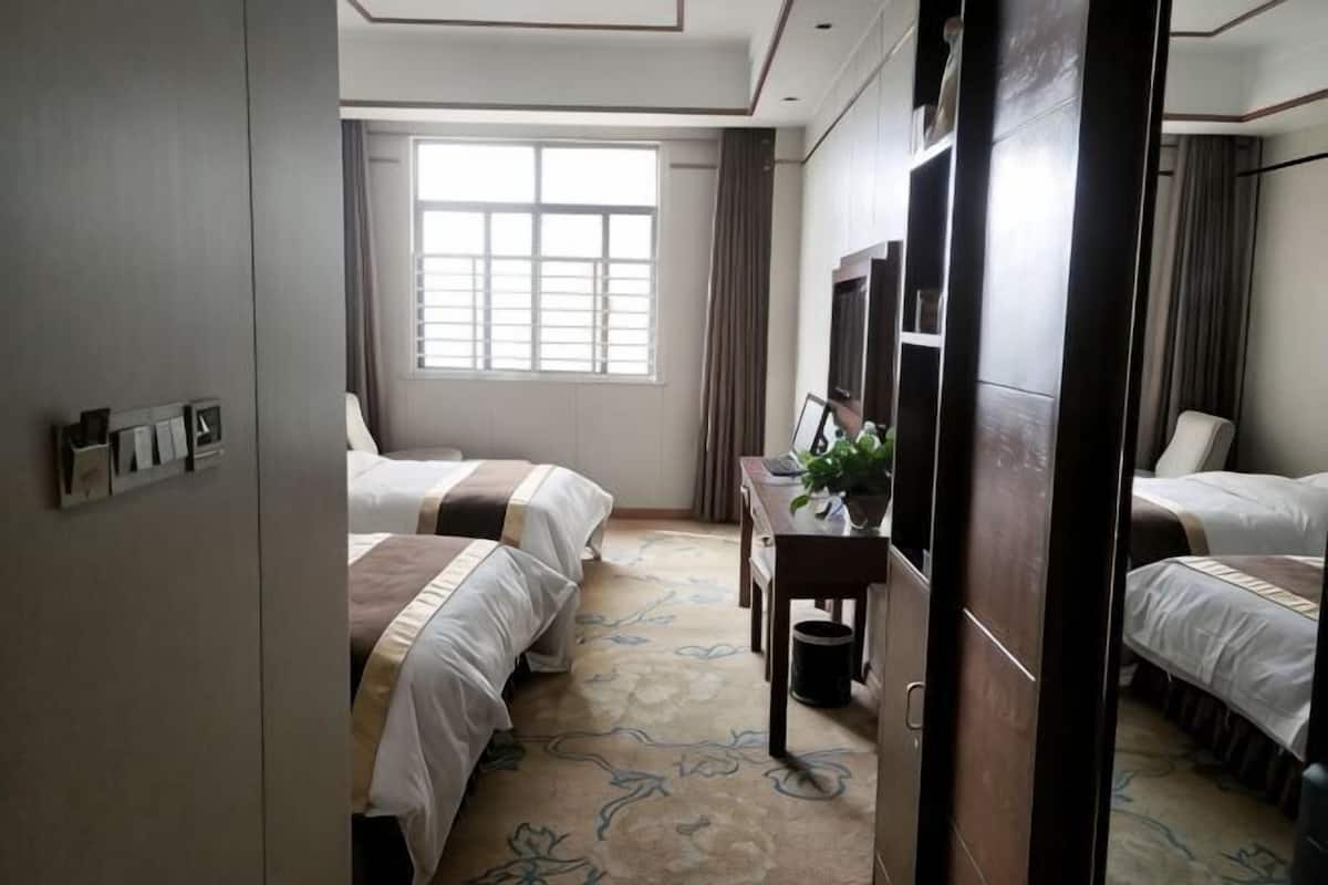 A hotel room with two beds, a desk with a plant, a TV, and a window with curtains.