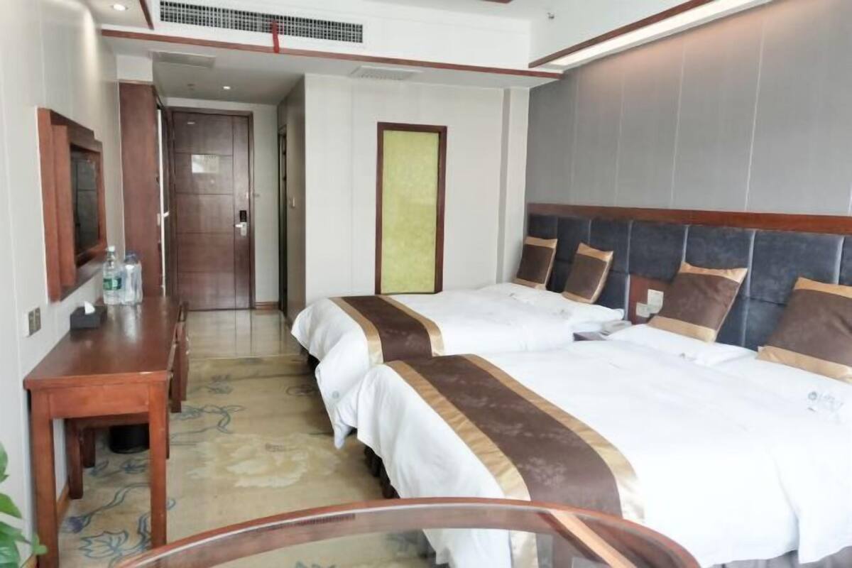 Una habitación de hotel con dos camas, un escritorio de madera, un espejo y un ventanal amplio.