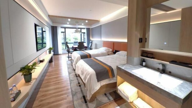 A modern hotel room with two beds, a large mirror, a vanity with a sink, and a desk with a chair. - Huarong Jasmine Hotel (Huarong)