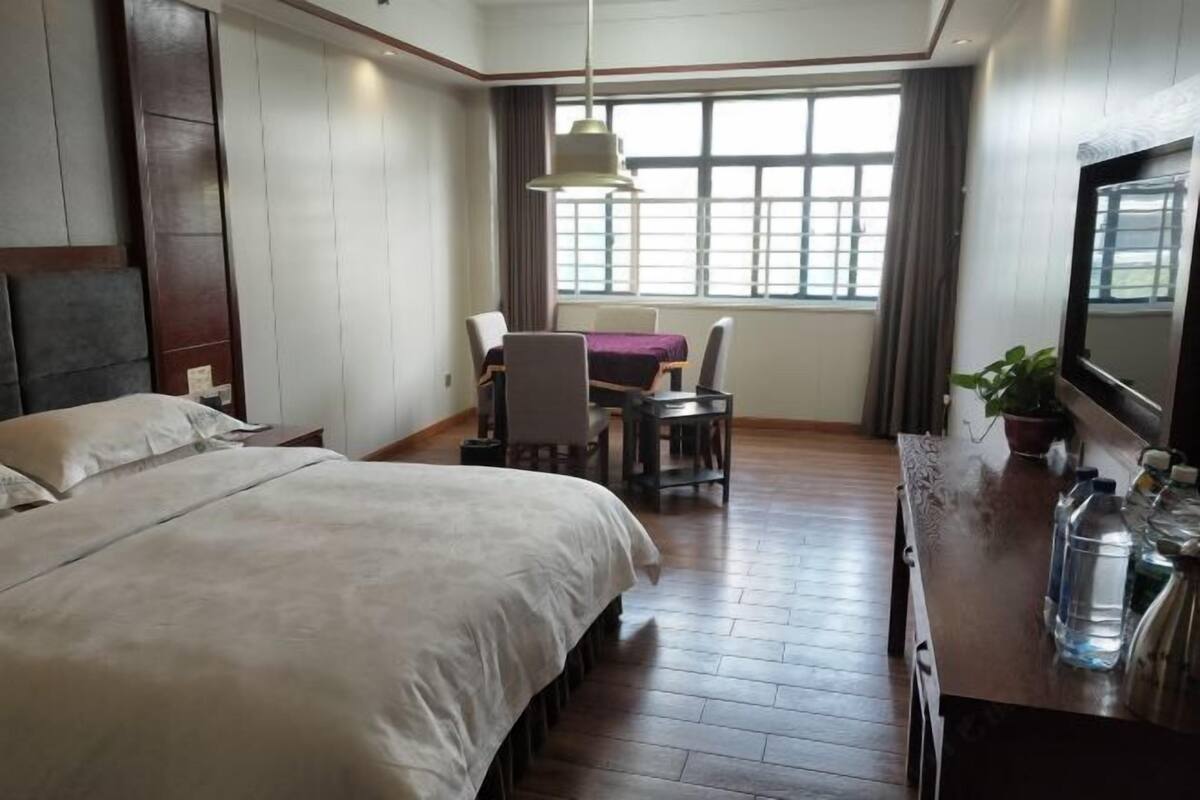 Una habitación de hotel con una cama grande, un escritorio con dos sillas, un televisor y una ventana con cortinas.