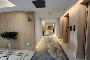 A hotel corridor with a carpeted floor, wooden walls, and a plant in the center. - Huarong Jasmine Hotel (Huarong)