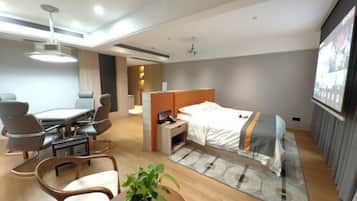 Una habitación de hotel moderna con una cama, un escritorio con sillas, una mesita y una planta.
