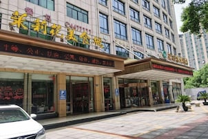 Un hotel con fachada moderna, varias entradas y un estacionamiento visible.