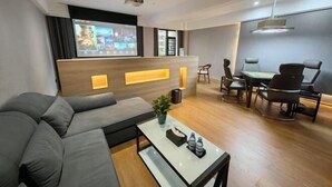 A modern hotel room with a sofa, a small table with a plant, a desk with a chair, and a large screen on the wall. - Huarong Jasmine Hotel (Huarong)