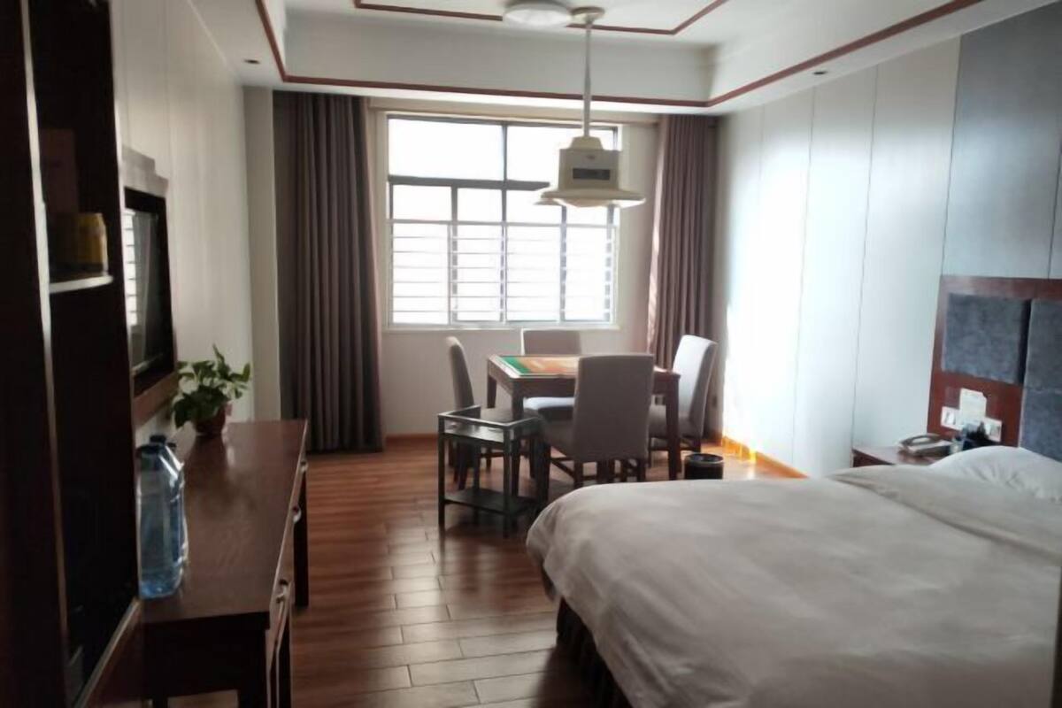 Habitación de hotel con una cama grande, un escritorio con silla, una mesita, una botella de agua y una ventana con cortinas.