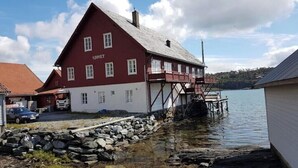 A red building with the name 'Sjostet' on the side, located by a body of water with a dock extending into the water. - Charming sea house with private sauna & jetty with direct access to the fjord (Vestland)