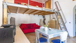 A loft-style room with a red couch, a glass table, and a ladder.