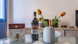 A hotel room with a table displaying a bottle of Chianti wine, a box of Cantuccini cookies, and a vase with tulips.