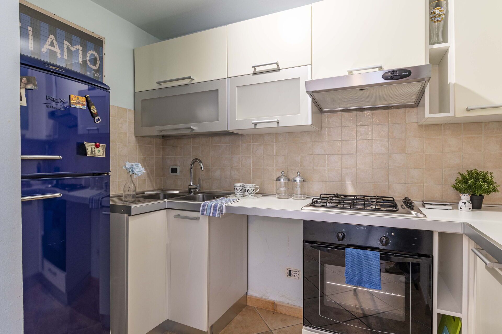 A modern kitchen with a blue refrigerator, white cabinets, a stainless steel sink, and a gas stove.