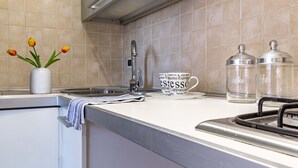 A kitchen with a tiled backsplash, a sink, a faucet, a vase with tulips, a coffee cup with coffee-related words, and two glass containers.