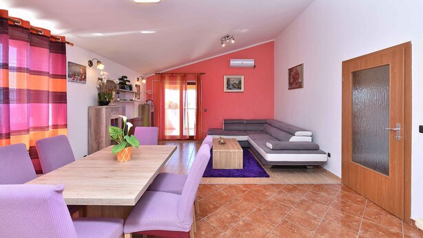 A living room with a wooden dining table, purple chairs, a sofa, and a wooden door.